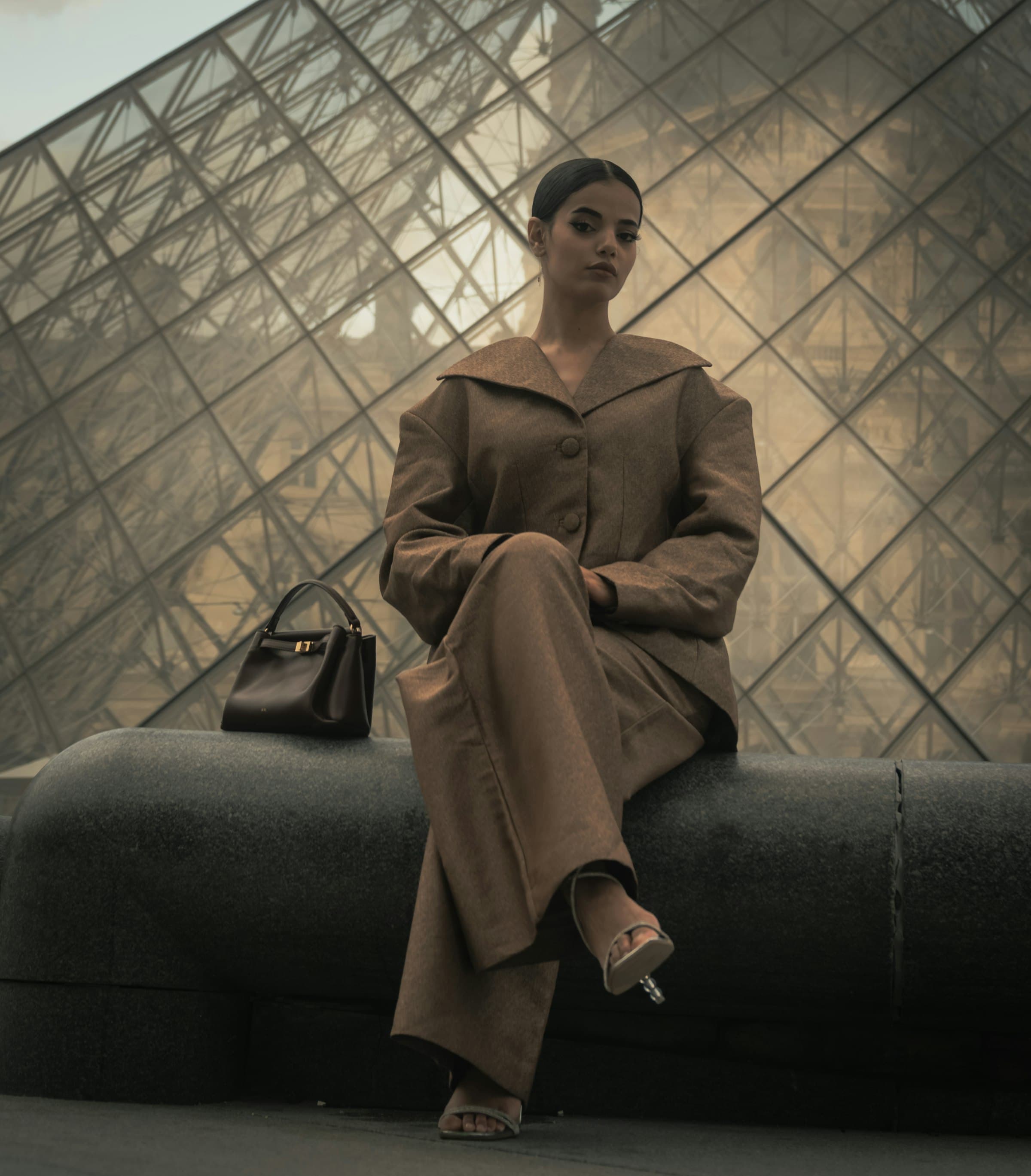 Model in an espresso suit seated in warm, raking light