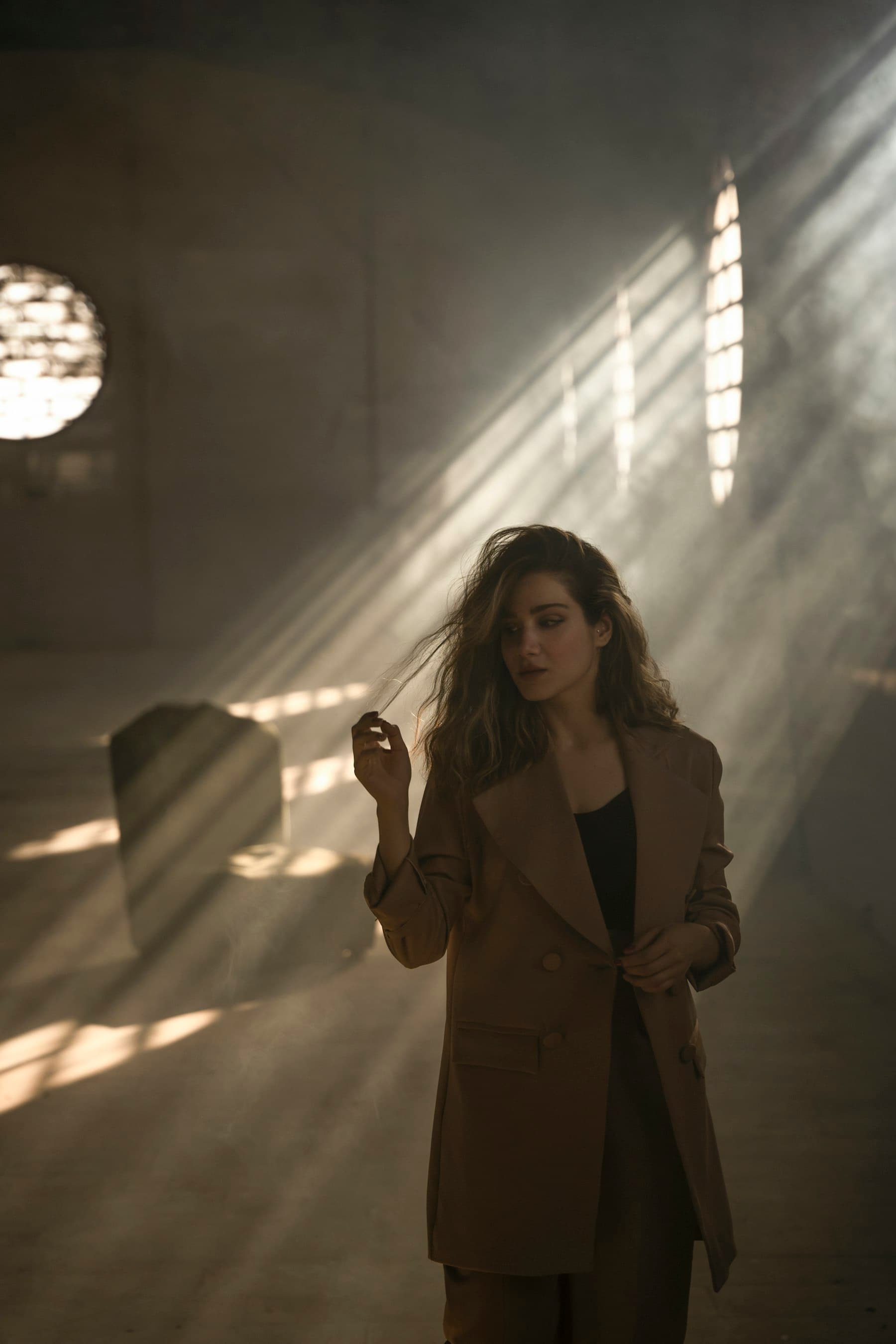 Model in an espresso wool coat seated on a stone plinth in raking autumn light