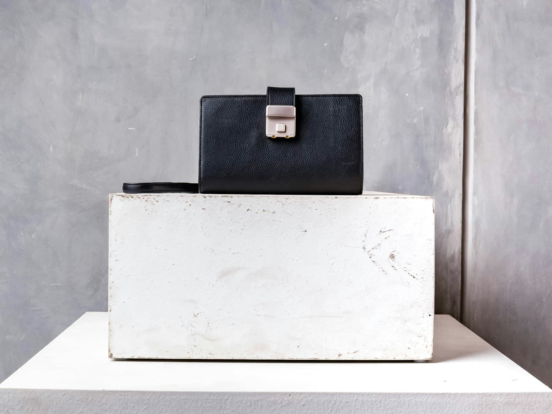 A black leather bag on a stone plinth beside dried branches
