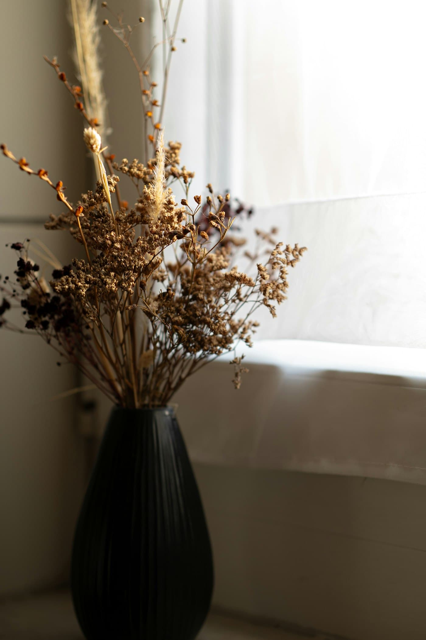 A black vase of dried blossoms on stacked books in raking light